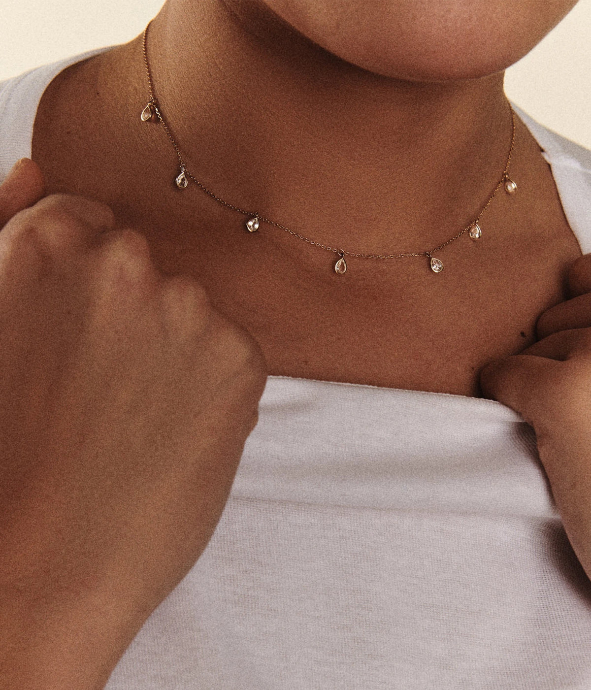 Close-up of a model wearing the Pascale Monvoisin Palerme White Sapphire Necklace at the collarbone with a pale grey top, hands resting at the chest