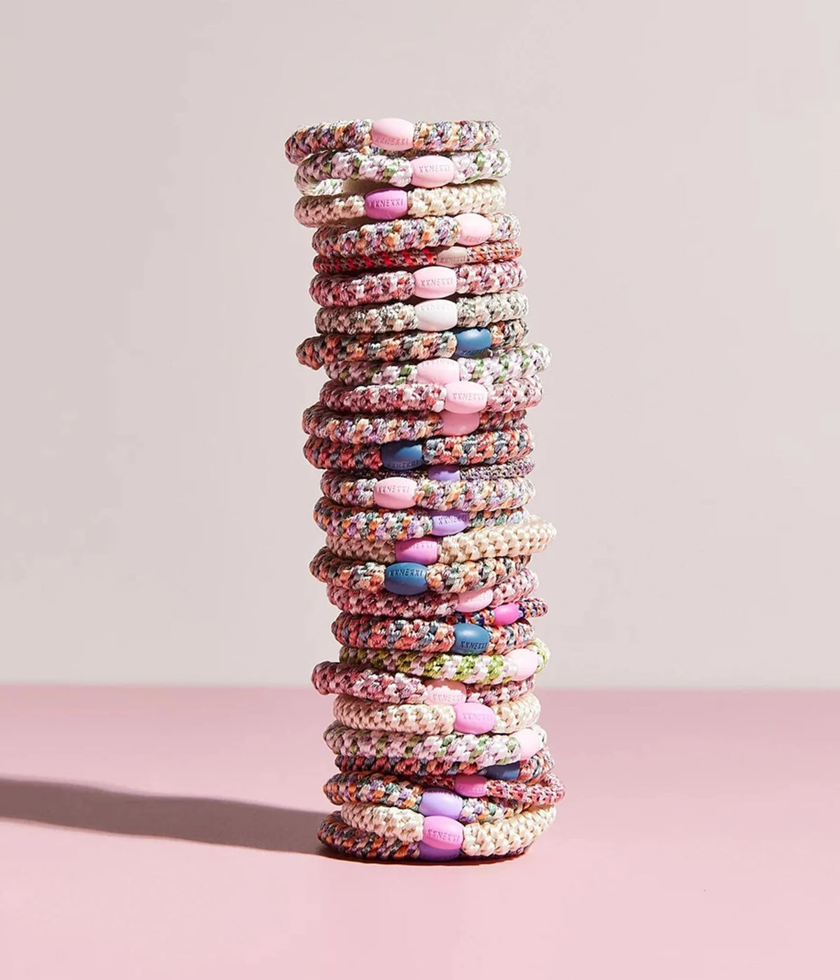 A tall stack of multicoloured braided hair ties with pink oval beads