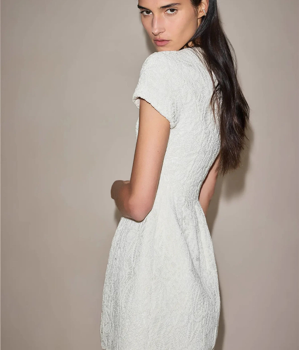 Rear three-quarter view of a model wearing the Alexis Regatta Dress In Floral Macrame looking over her shoulder, showing the short sleeves and fitted back