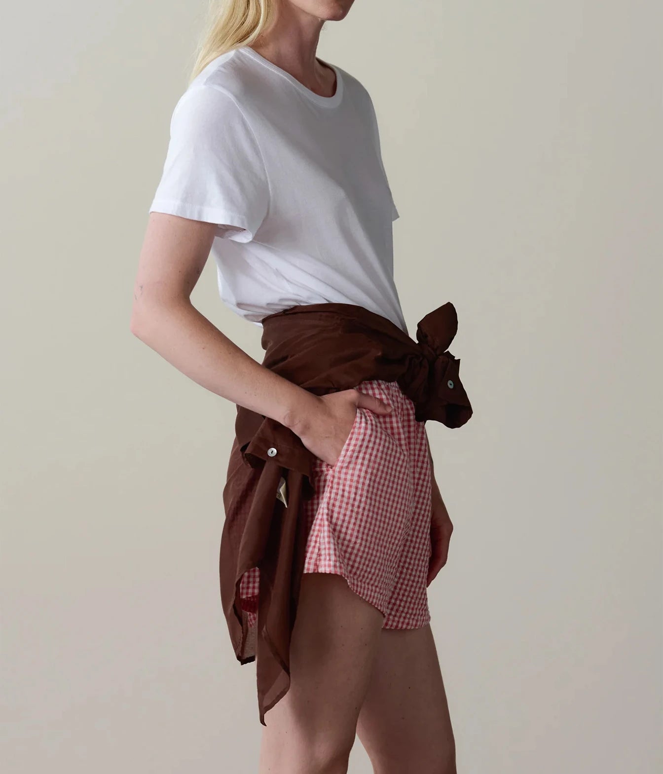 Model wearing pink gingham check shorts with a white t-shirt, side profile view showing the relaxed fit.