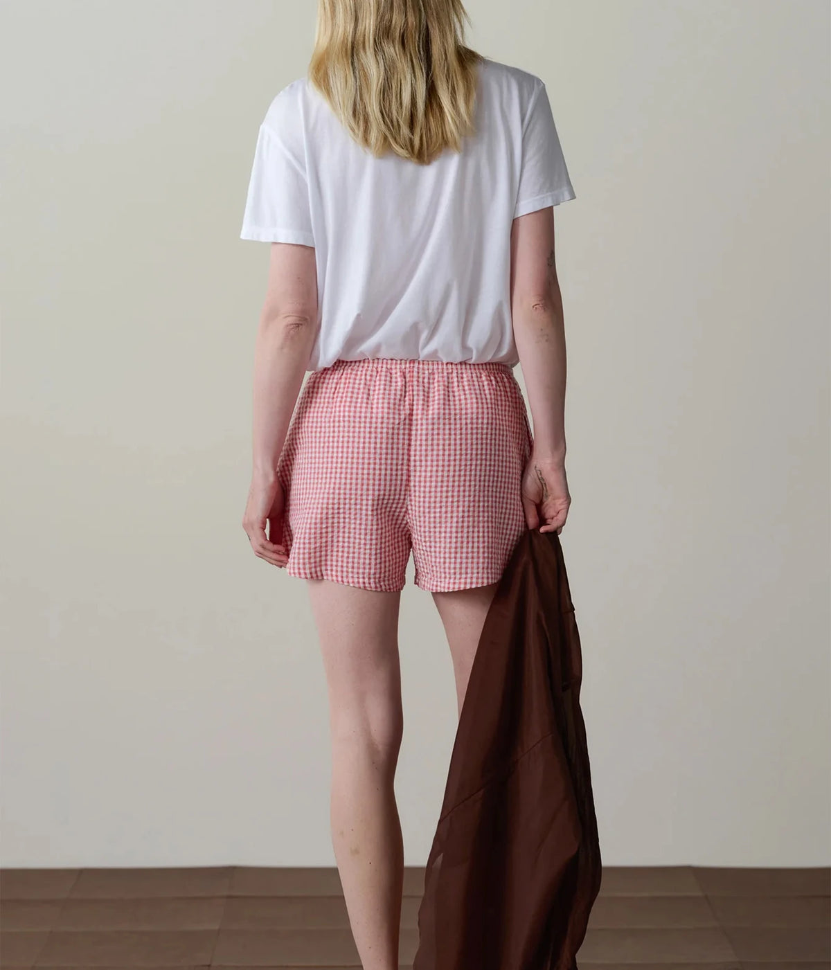 Model wearing pink gingham check shorts with a white t-shirt, back view showing the relaxed fit.