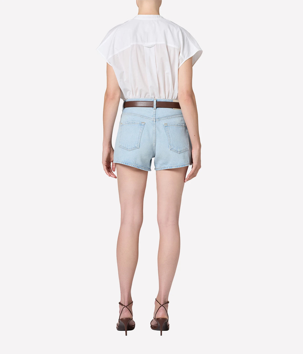 Full-length back view of a model wearing the Citizens Of Humanity Marlow Welt Pocket Short in Lasso with a white cap-sleeve top tucked in, a brown leather belt and dark strappy heeled sandals