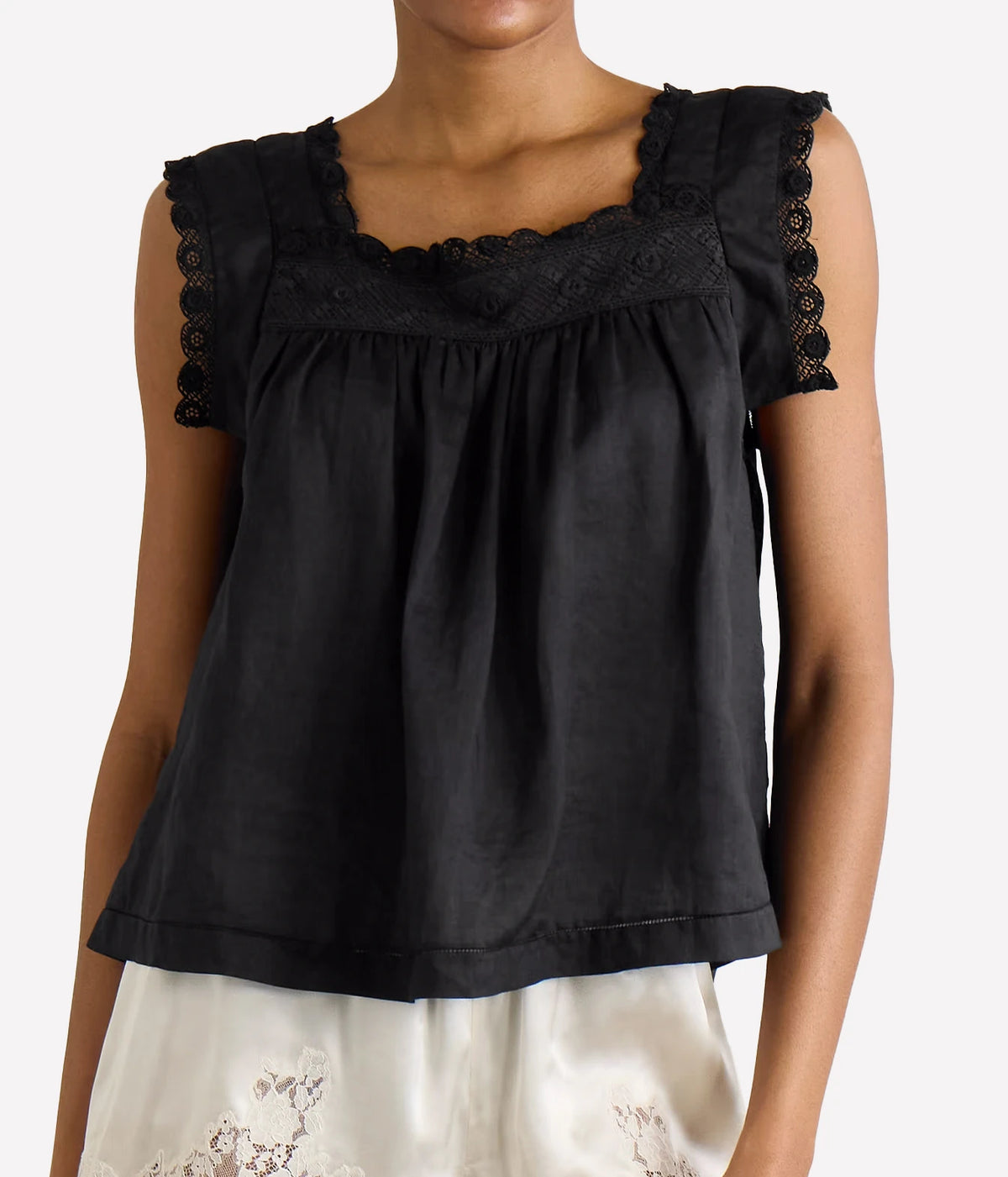 A black sleeveless top with a square neckline, delicate lace trim along the shoulders, and a gathered front, shown on a model against a light gray background.