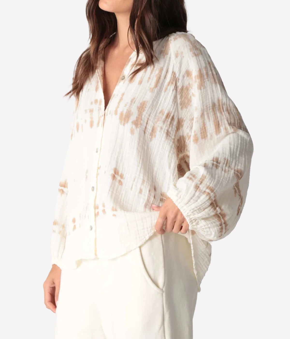 Side angle of a model with a hand in her pocket in the Electric Rose Winnie Horizon Shirt in Dune Ivory, showing the dropped shoulder, full sleeve and curved hem, with ivory trousers