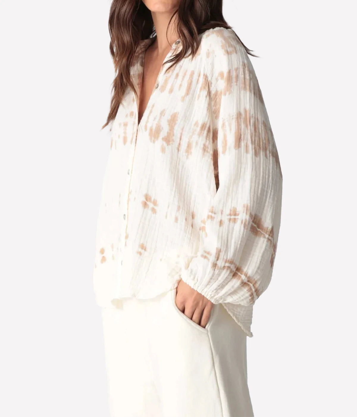 Three-quarter side view of a model wearing the Electric Rose Winnie Horizon Shirt in Dune Ivory, showing the oversized fit, open V neckline and gathered cuffs, with ivory trousers