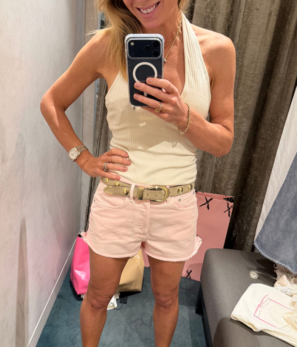 A mirror selfie of Nicky wearing a cream ribbed halter top and light pink Citizens of Humanity Marlow Denim Short with a gold belt. She is standing in a fitting room.