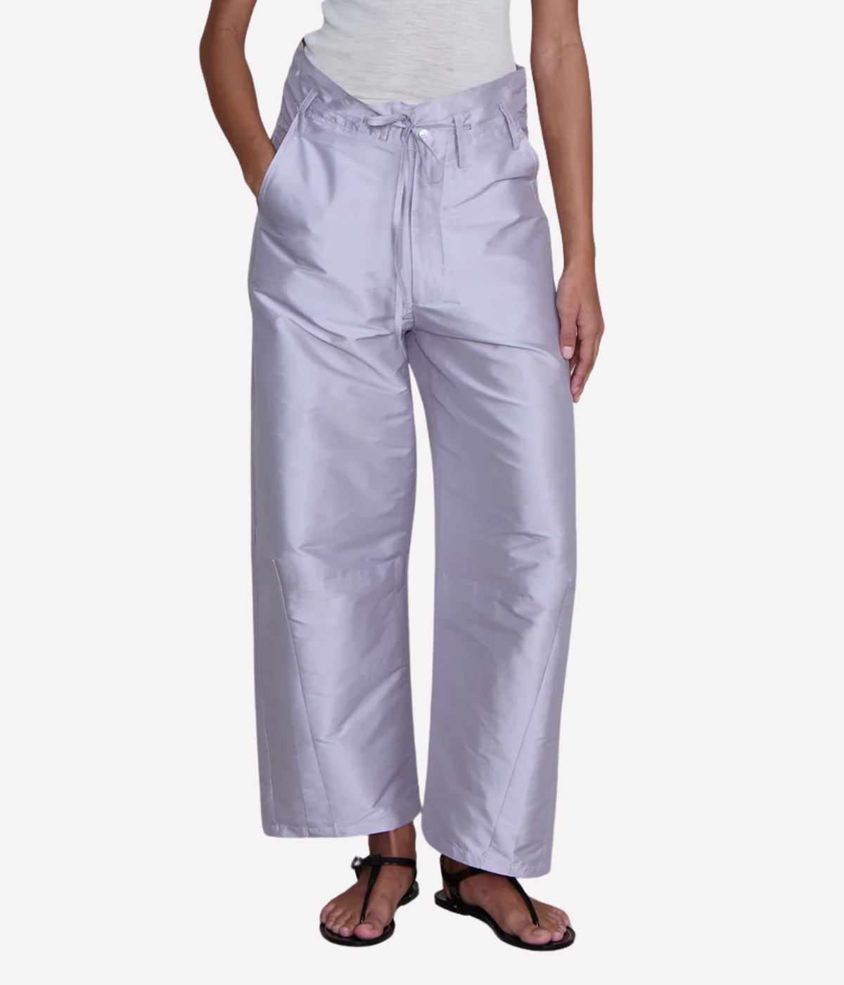 Close-up front view of a model wearing the Chan Luu Techno Taffeta Barrel Pant in Lilac with a grey marl top and black thong sandals, showing the tied front waist, button closure and curved barrel legs