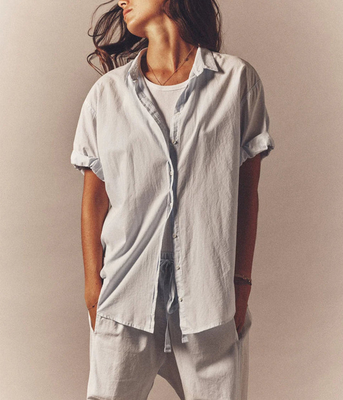 Model wearing the Xirena Channing Shirt in Skylight open over a white ribbed tank with light drawstring pants, sleeves rolled and hands in pockets
