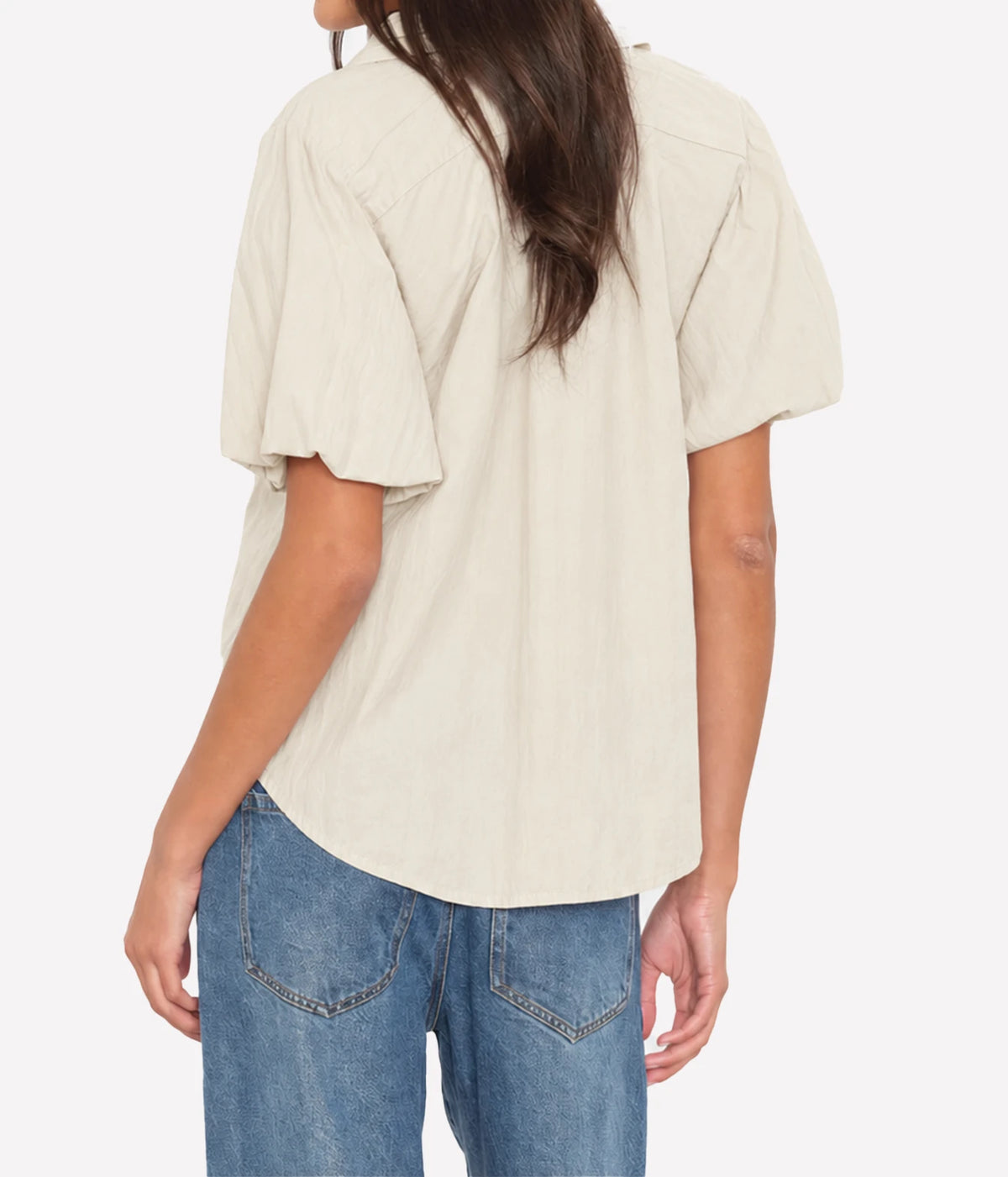 Back view of a model wearing the Xirena Lyla Shirt in Parchment untucked over mid-wash blue jeans, showing the voluminous balloon sleeves and curved hem