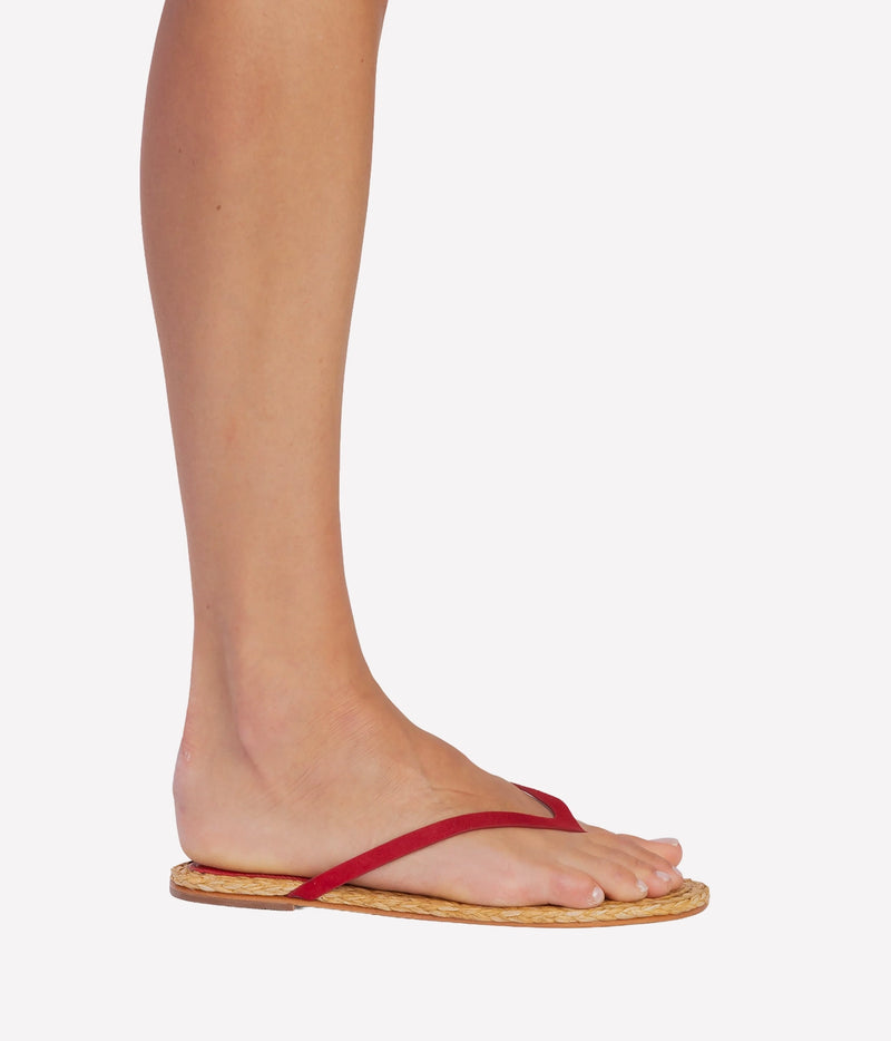 A side-profile view of a person's foot wearing a red thong sandal with a natural woven sole - Alaya Sandal in Cherry Suede