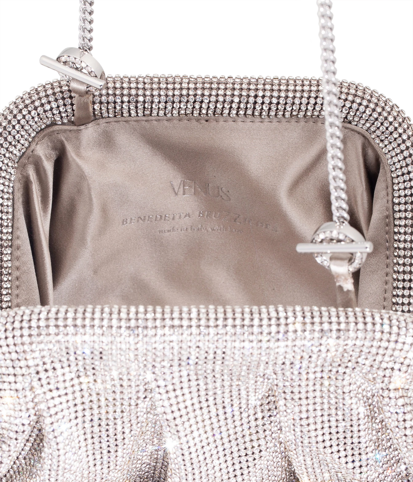 Close-up of the interior of a silver rhinestone clutch bag, showing a satin lining with the brand name