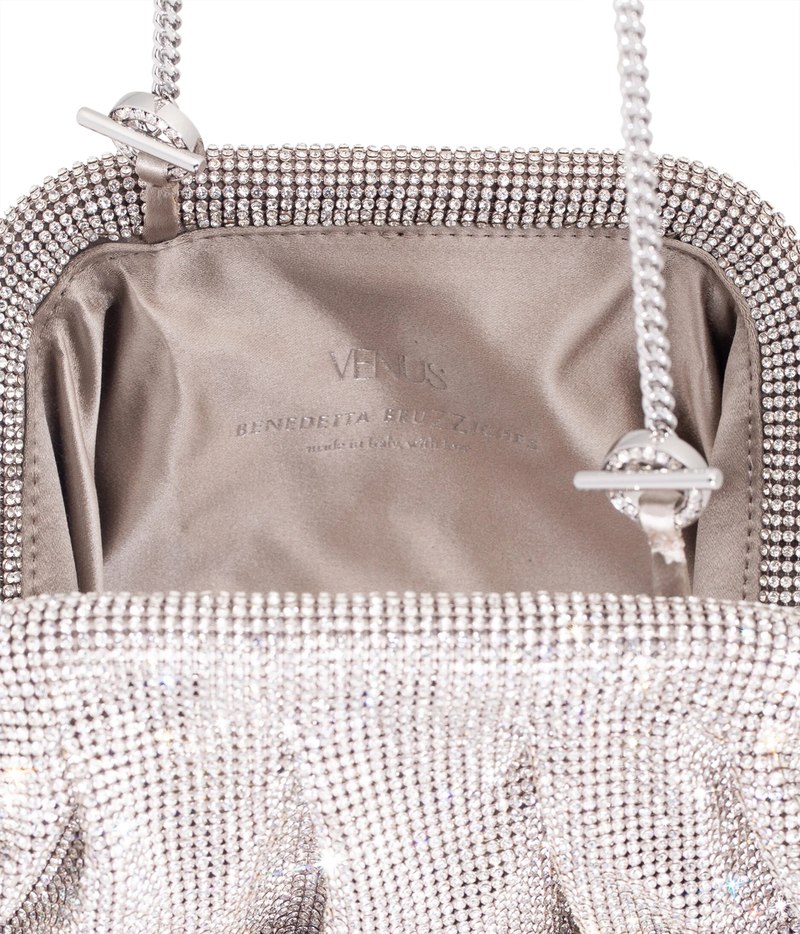 Close-up of the interior of a silver rhinestone clutch bag, showing a satin lining with the brand name