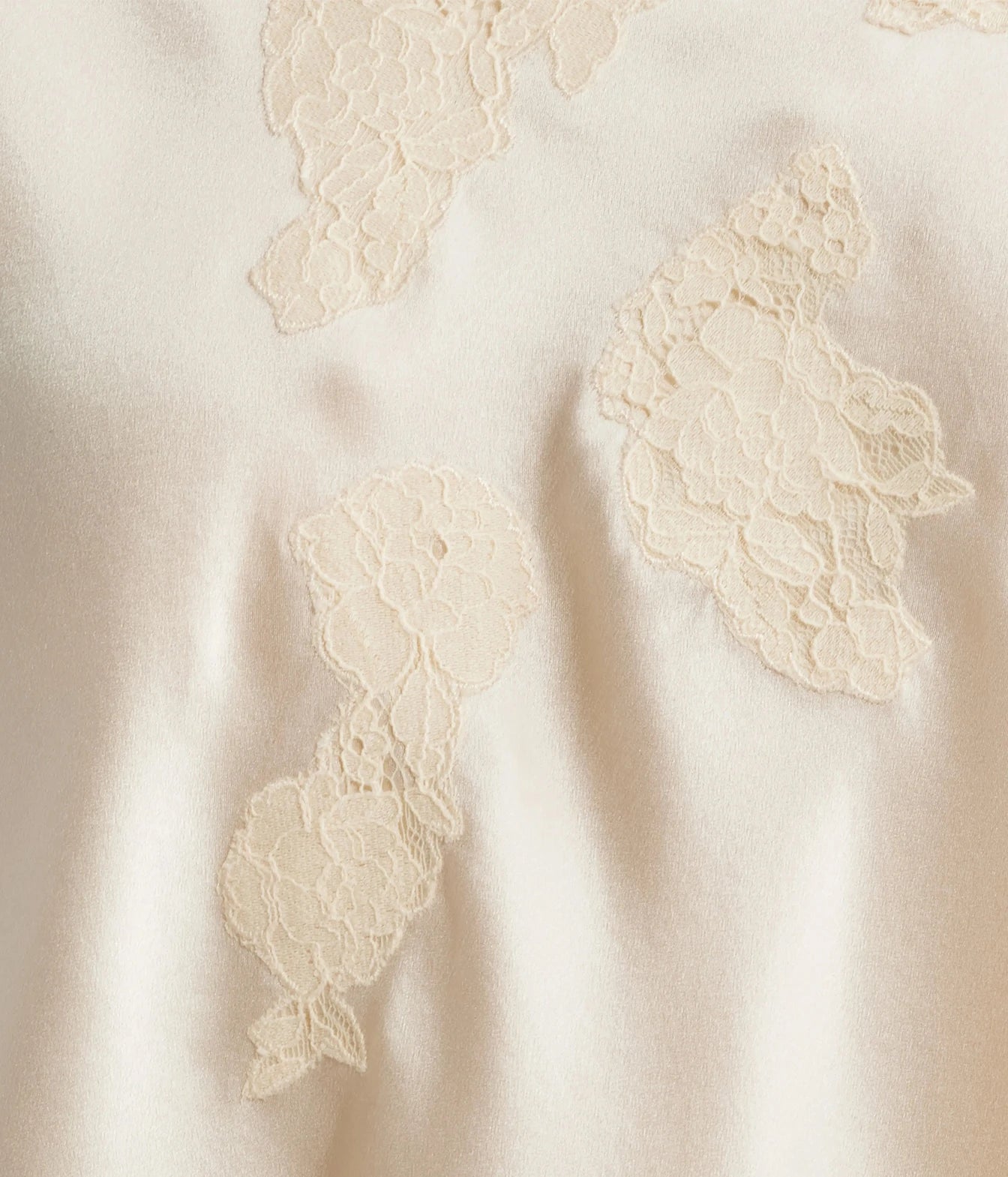 Close-up of a cream satin fabric with embroidered floral lace appliques.