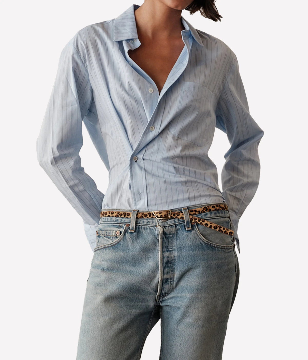Model wearing the CISSA Daily Shirt in Blue Needle with the collar open, tucked into light-wash jeans with a leopard-print belt, showing the fine blue pinstripe
