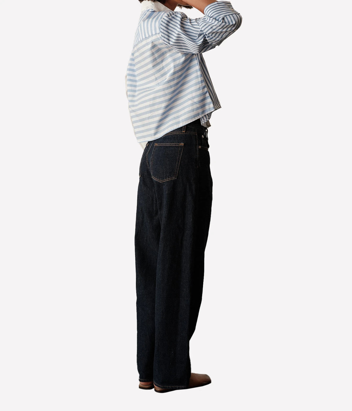 Side profile of a model wearing the CISSA Shorty Shirt in Stripe Scrappy with dark wide-leg jeans, one hand raised to her hair, showing the boxy cropped fit