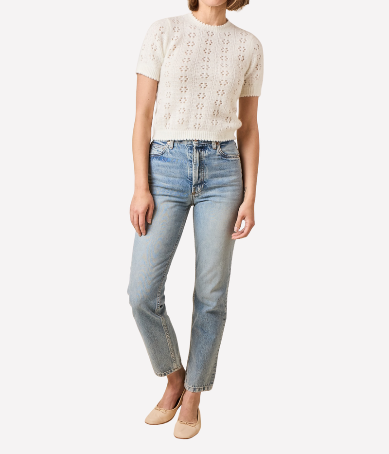 Person wearing a white lace top and light blue jeans on a white background