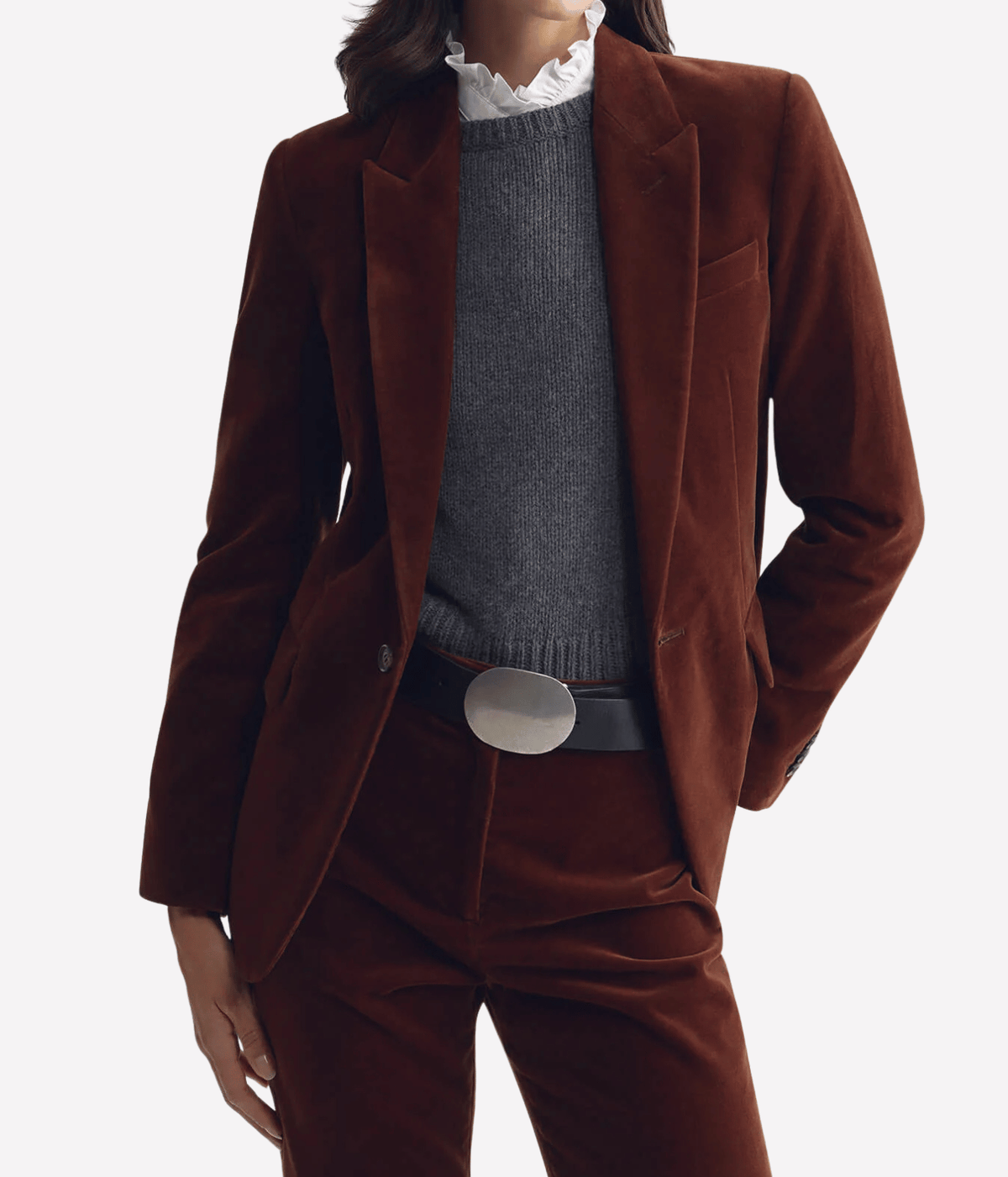 Model wearing the Nili Lotan Anabel Tailored Jacket in Burnt Sienna open over a charcoal knit and white ruffle-collar shirt with matching trousers, a silver oval belt buckle and one hand in pocket