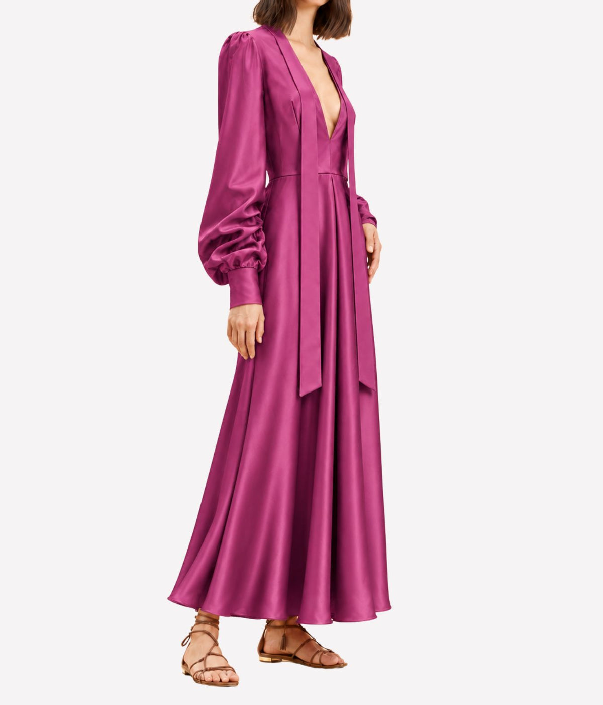 Three-quarter side view of a model wearing the Raquel Diniz Valerie Dress In Fuchsia with tan strappy sandals, showing the flowing skirt and gathered sleeves