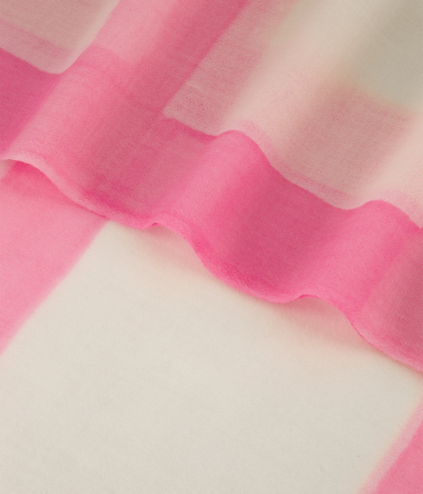 A close-up of a sheer pink fabric draped over a white textured surface, showing the soft, semi-transparent material and wavy folds.