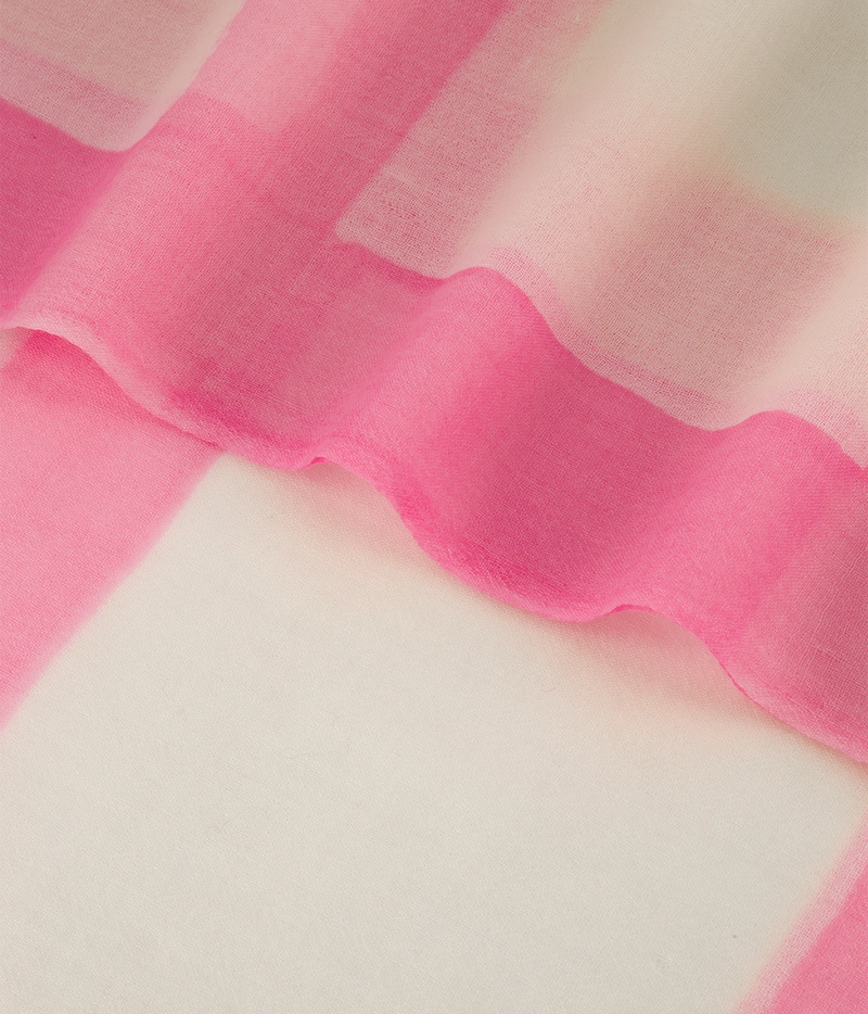 A close-up of a sheer pink fabric draped over a white textured surface, showing the soft, semi-transparent material and wavy folds.