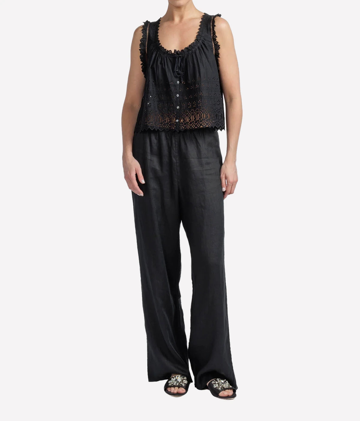 Person wearing a black eyelet blouse short sleeve and dark pants on a white background