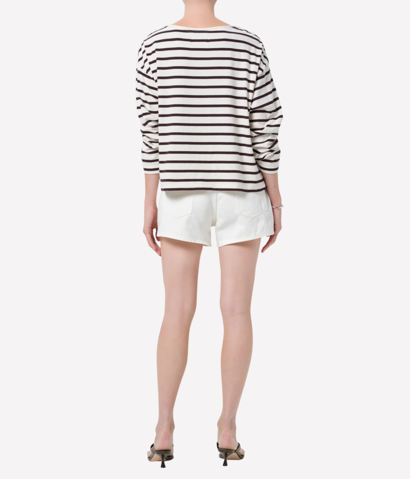 A model shown from the back wearing a black and white horizontally striped long-sleeve top, white shorts, and black high-heeled sandals against a light gray background.