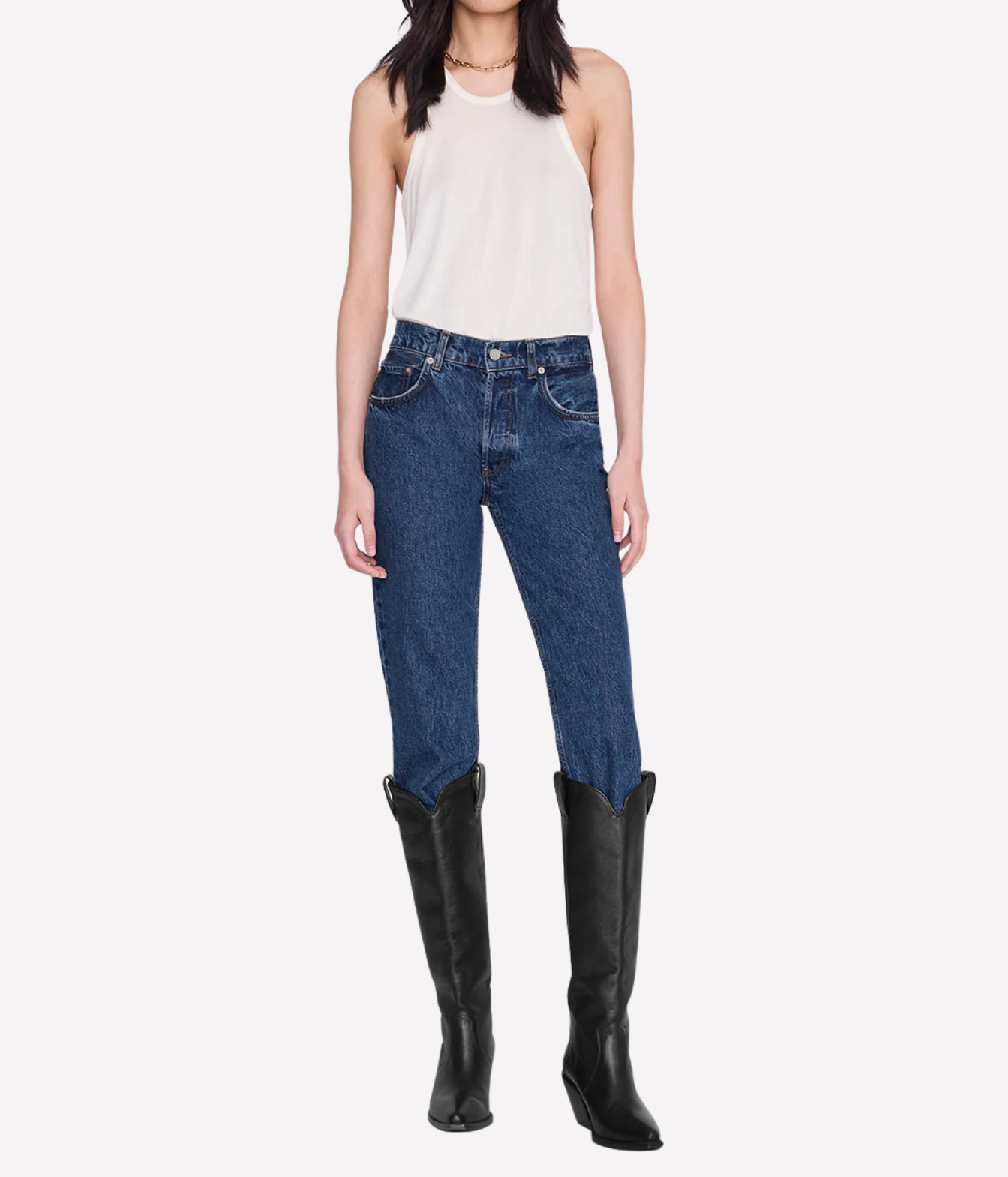 A model wearing a white sleeveless top, blue denim jeans, and black knee-high leather boots, shown against a plain light gray studio background.