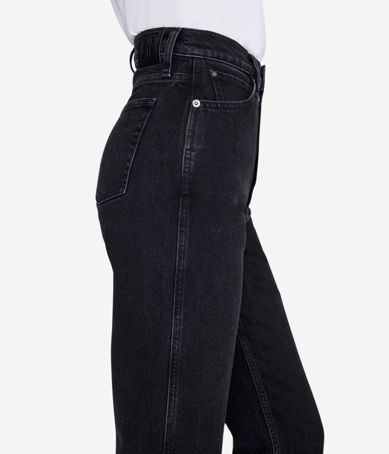 Close-up side view of a person wearing black denim jeans with a white top visible at the waist, against a light gray studio background.