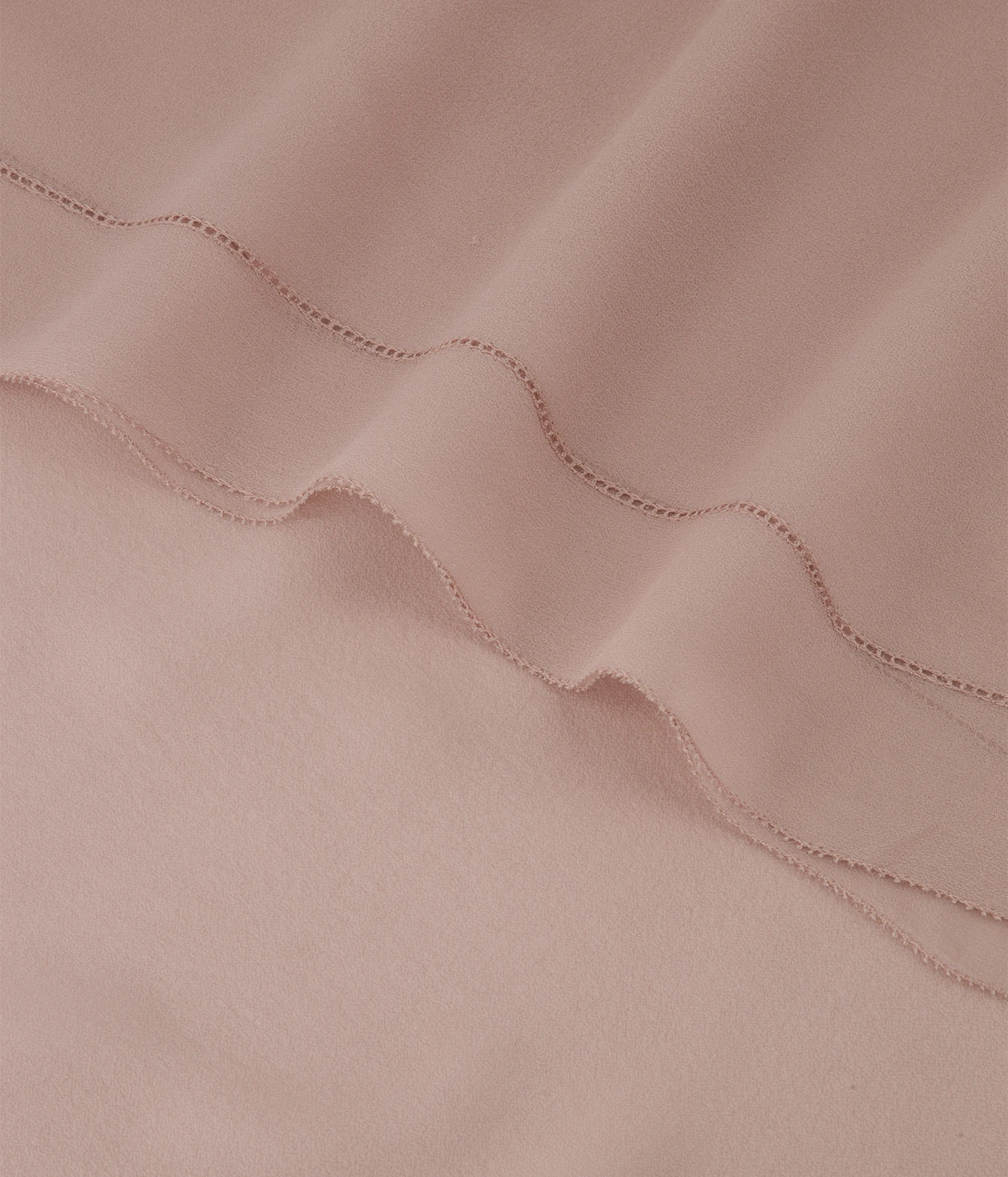 A close-up of soft blush pink fabric with a wavy stitched seam running diagonally across the frame.