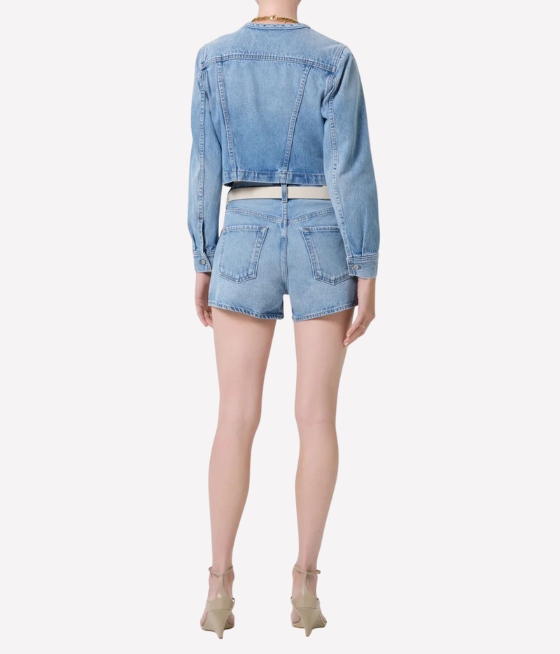 A model shown from the back wearing a light blue cropped denim jacket and matching denim shorts, paired with beige high-heeled sandals against a plain light gray background.