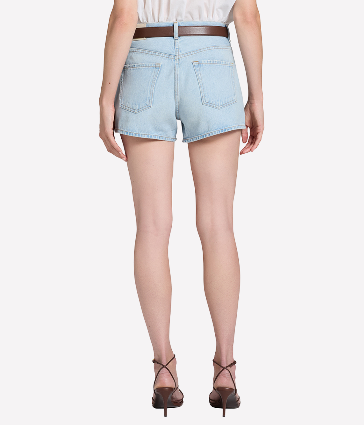Back view of a model wearing the Citizens Of Humanity Marlow Welt Pocket Short in Lasso with a brown leather belt, showing the back pockets and clean hem, paired with dark strappy heeled sandals