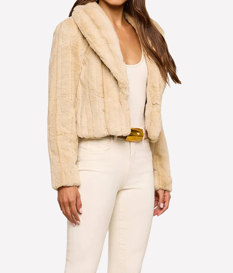 A woman wearing a L'AGENCE Davy Faux Fur Jacket in Latte Striped Fur styled with a white tank top, cream-coloured jeans, and a gold belt, against a plain white studio background.