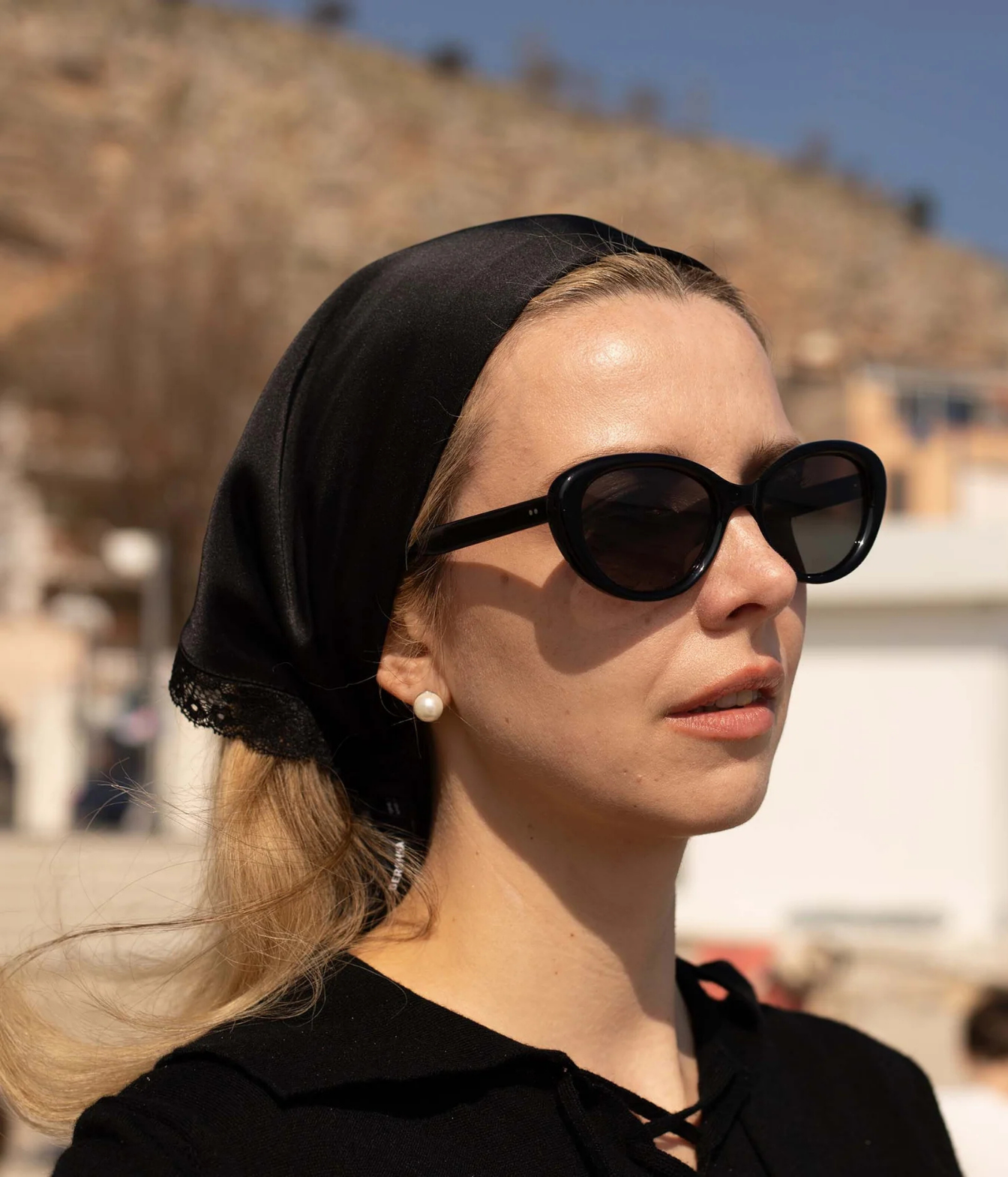 A woman in profile wearing black cat-eye sunglasses, a black headscarf