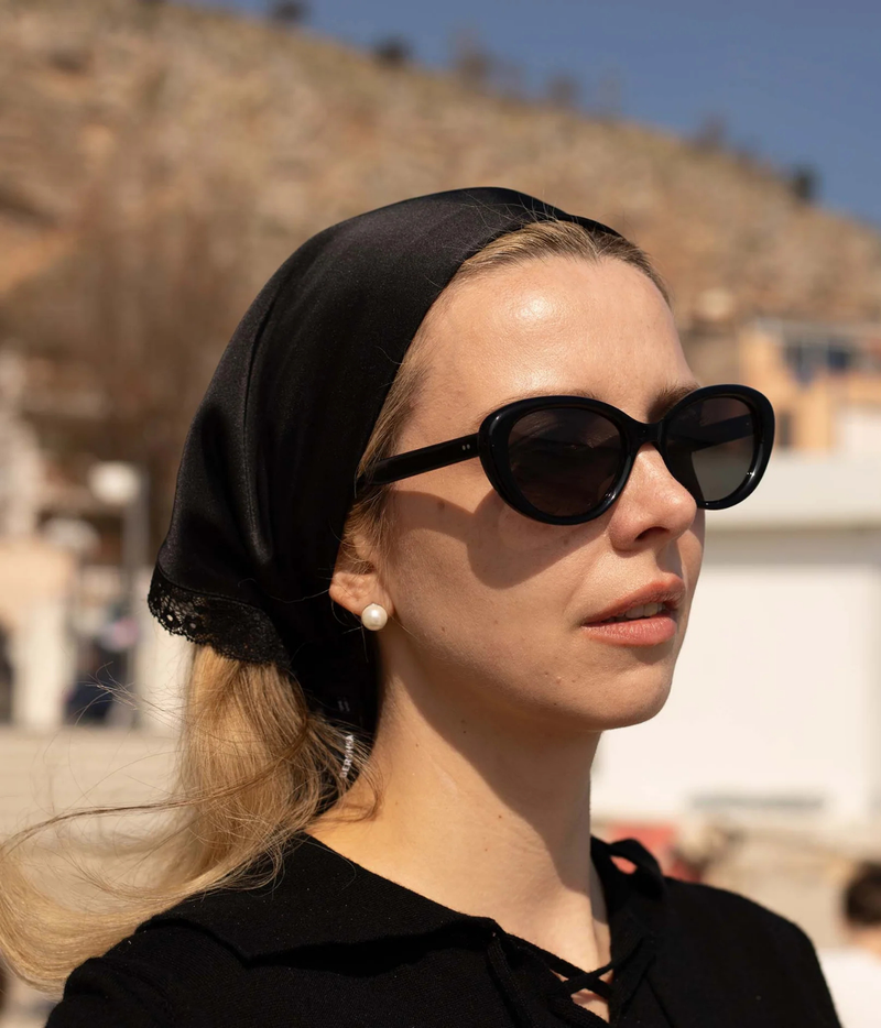 A woman in profile wearing black cat-eye sunglasses, a black headscarf