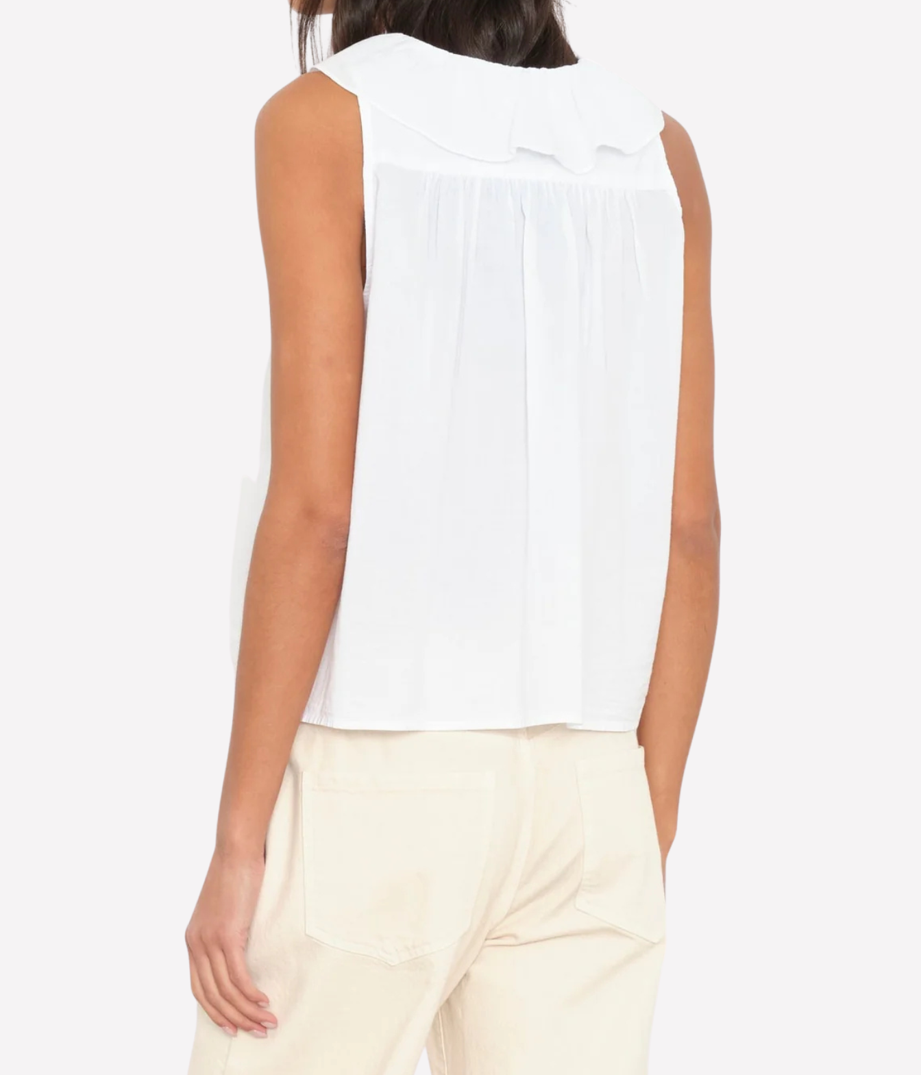 A woman shown from the back wearing a sleeveless white blouse with a wide collar and gathered back, paired with light beige pants, against a plain white background.