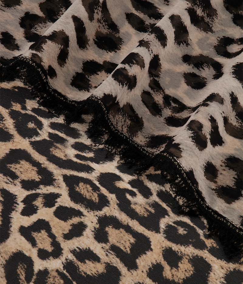 Leopard print fabric with black and beige animal spots, draped to show texture and a black fringed edge.