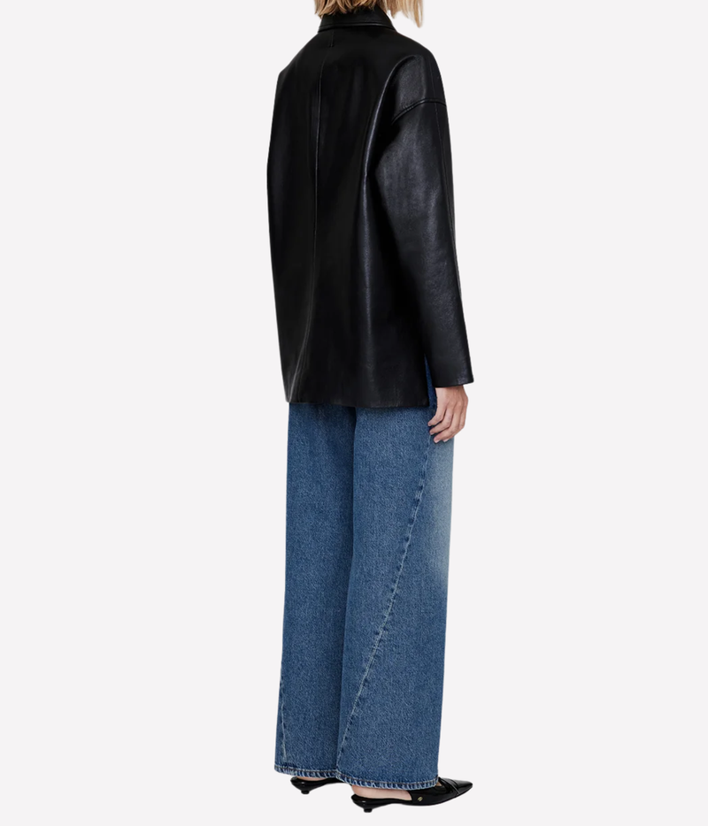A model shown from the back wearing a black leather jacket, wide-leg blue denim jeans, and black pointed flats against a plain white background.
