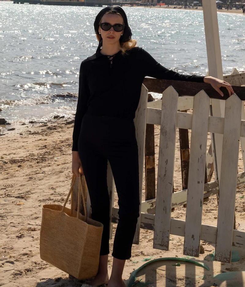 A woman stands on a sandy beach next to a white wooden lifeguard stand