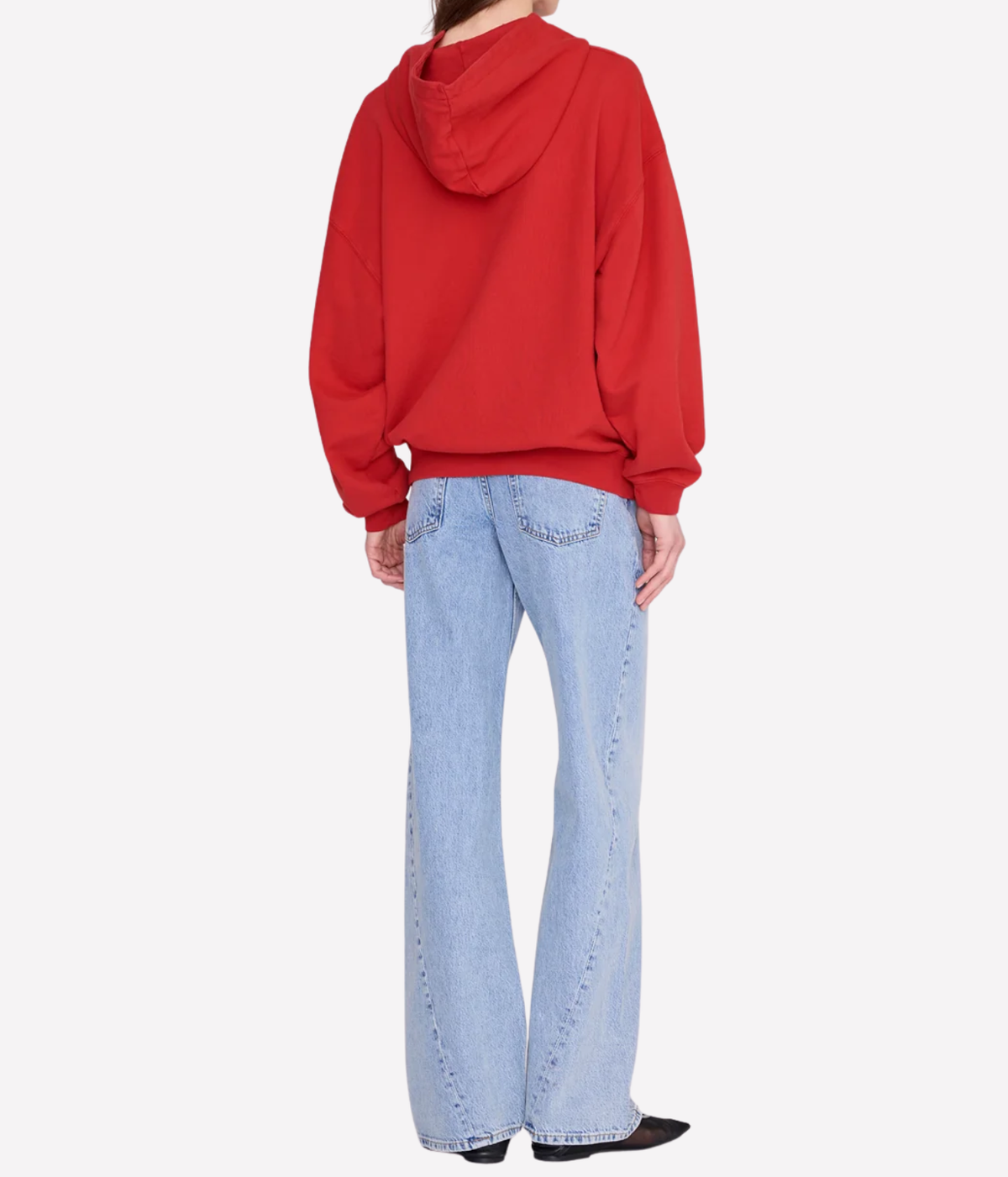 A model shown from the back wearing a bright red pullover hoodie and light-wash blue flare jeans, set against a plain light gray studio background.