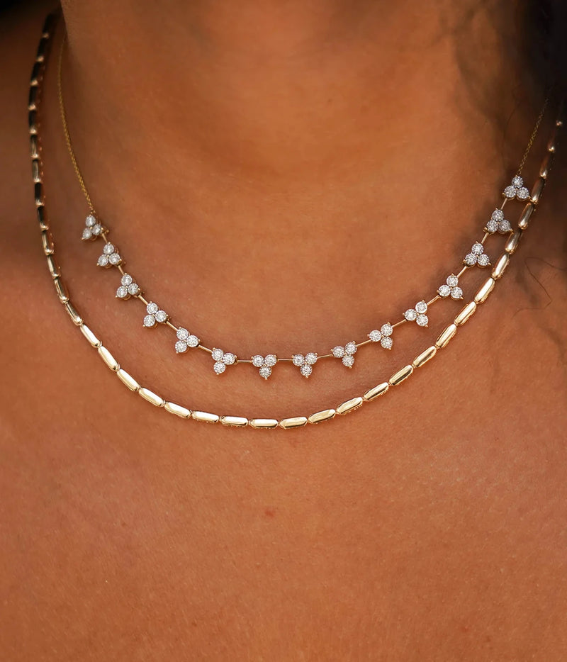 Model wearing the Dana Rebecca Designs Ava Bea Interval Trio Tennis Necklace in 14k Yellow Gold layered above a fine gold chain necklace on a bare neckline