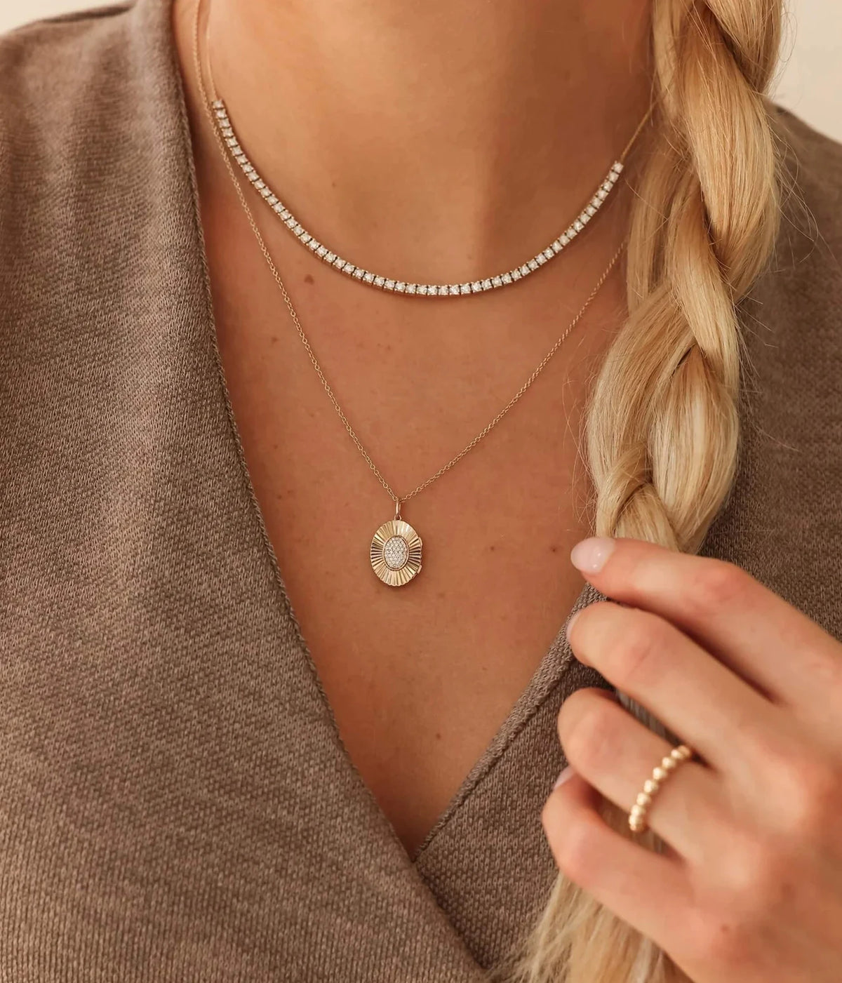 Model wearing the Dana Rebecca Designs Teddi Paige Oval Locket Necklace in 14k Yellow Gold layered beneath a flat gold chain with a brown knit top and a gold ring