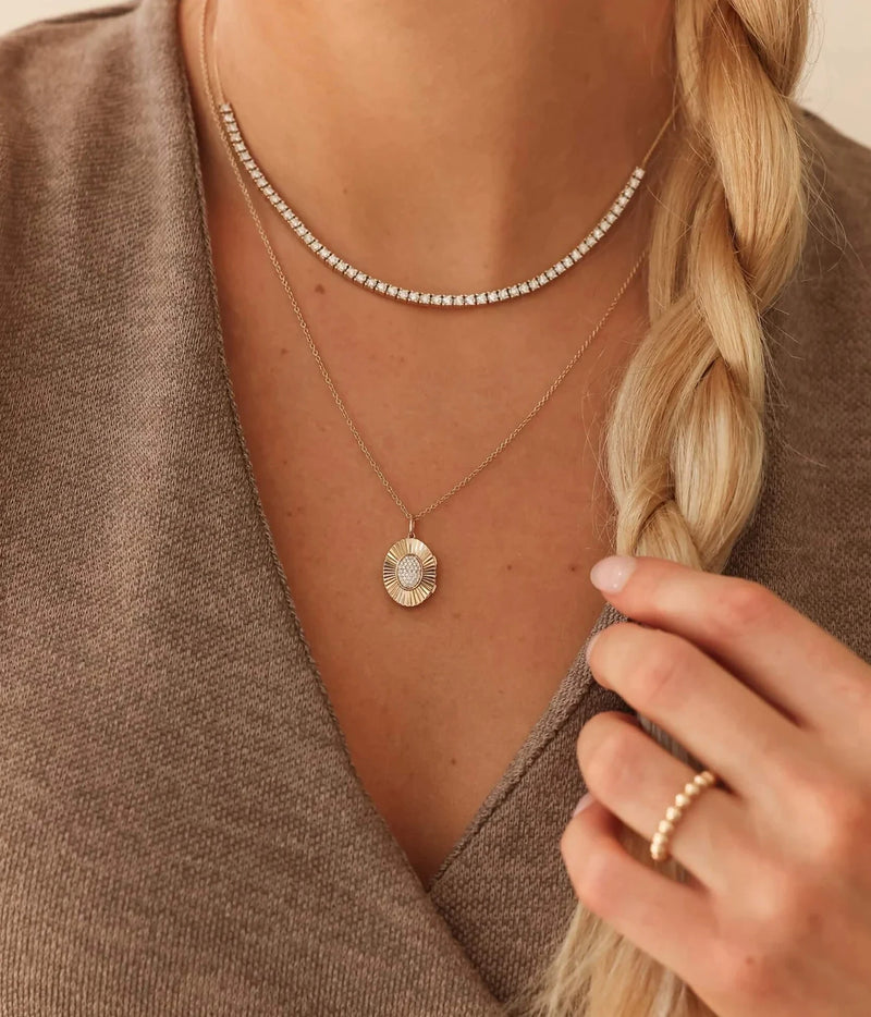 Model wearing the Dana Rebecca Designs Teddi Paige Oval Locket Necklace in 14k Yellow Gold layered beneath a flat gold chain with a brown knit top and a gold ring
