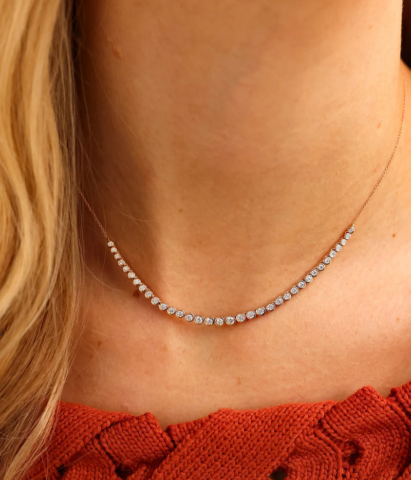 Model wearing the Dana Rebecca Designs Lulu Jack Graduating Bezel Tennis Necklace in 14k Yellow Gold at the collarbone with a rust-red textured top