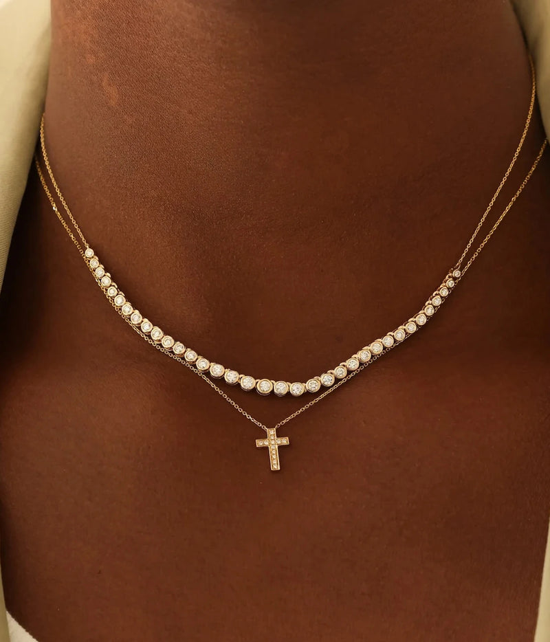 Model wearing the Dana Rebecca Designs Lulu Jack Graduating Bezel Tennis Necklace in 14k Yellow Gold layered above a fine gold chain with a small cross pendant