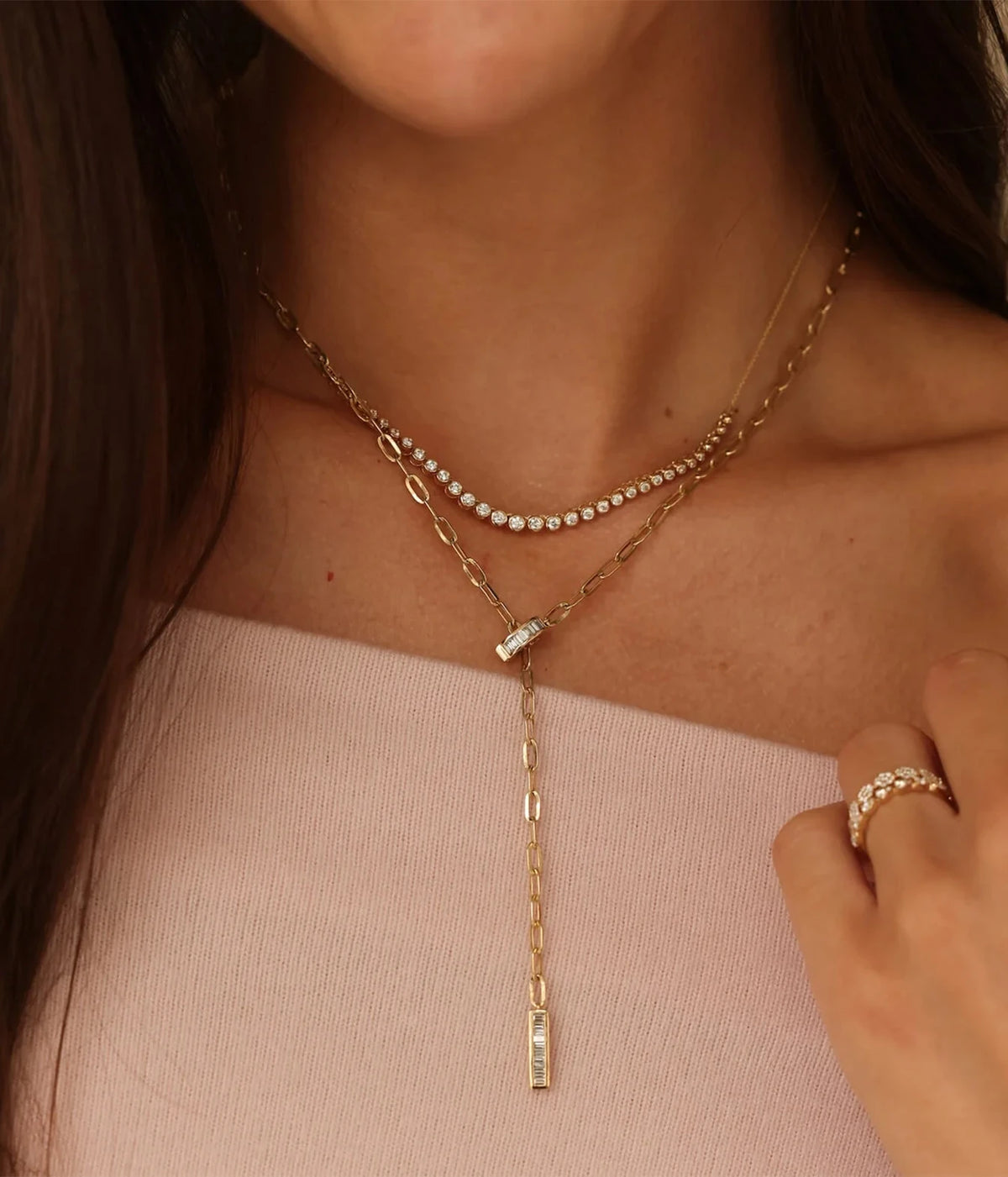 Model wearing the Dana Rebecca Designs Lulu Jack Graduating Bezel Tennis Necklace in 14k Yellow Gold layered with a gold drop lariat necklace, a pale pink top and gold rings