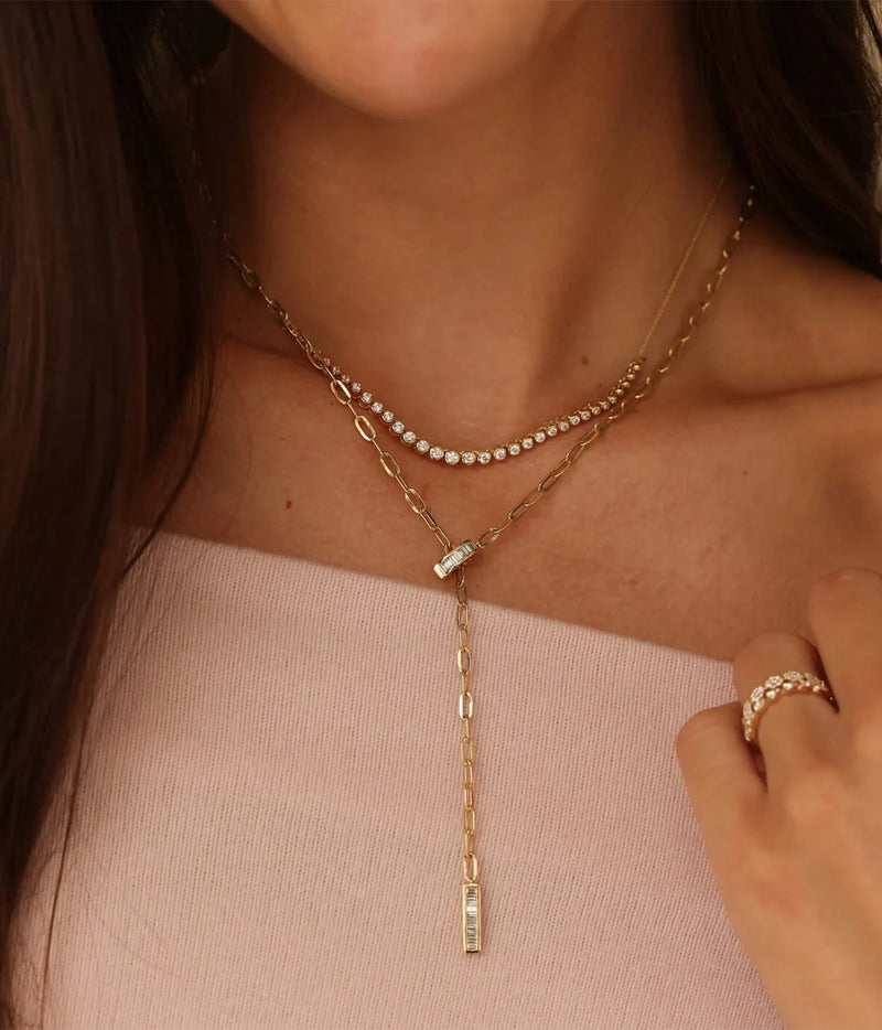 Model wearing the Dana Rebecca Designs Lulu Jack Graduating Bezel Tennis Necklace in 14k Yellow Gold layered with a gold drop lariat necklace, a pale pink top and gold rings
