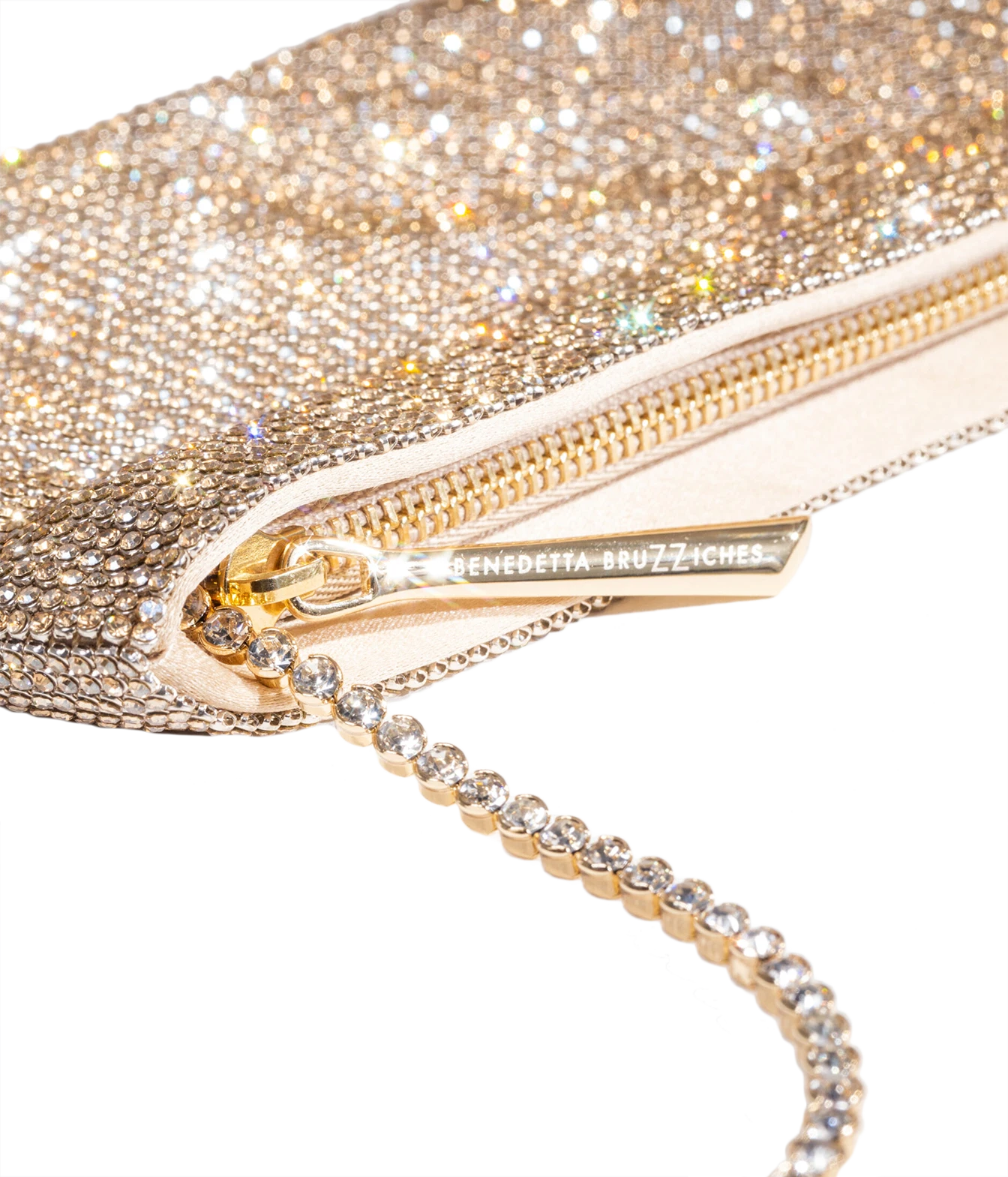 Close-up of a glittery gold evening clutch bag with a rhinestone-embellished chain strap and a gold zipper pull engraved with the brand name Benedetta Bruzziches.