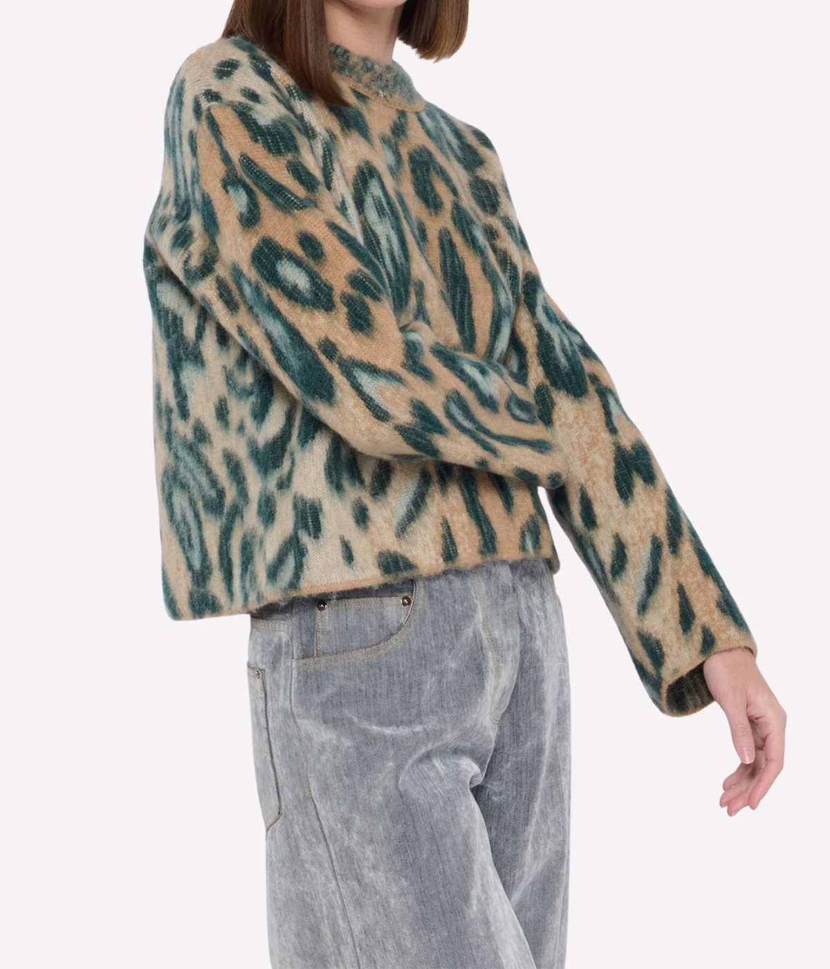 Model mid-stride in the forte forte Brit Leopard Jacquard Gauzed Alpaca Sweater in Woods with one arm swinging out, showing the boxy cropped fit over grey corduroy wide-leg trousers