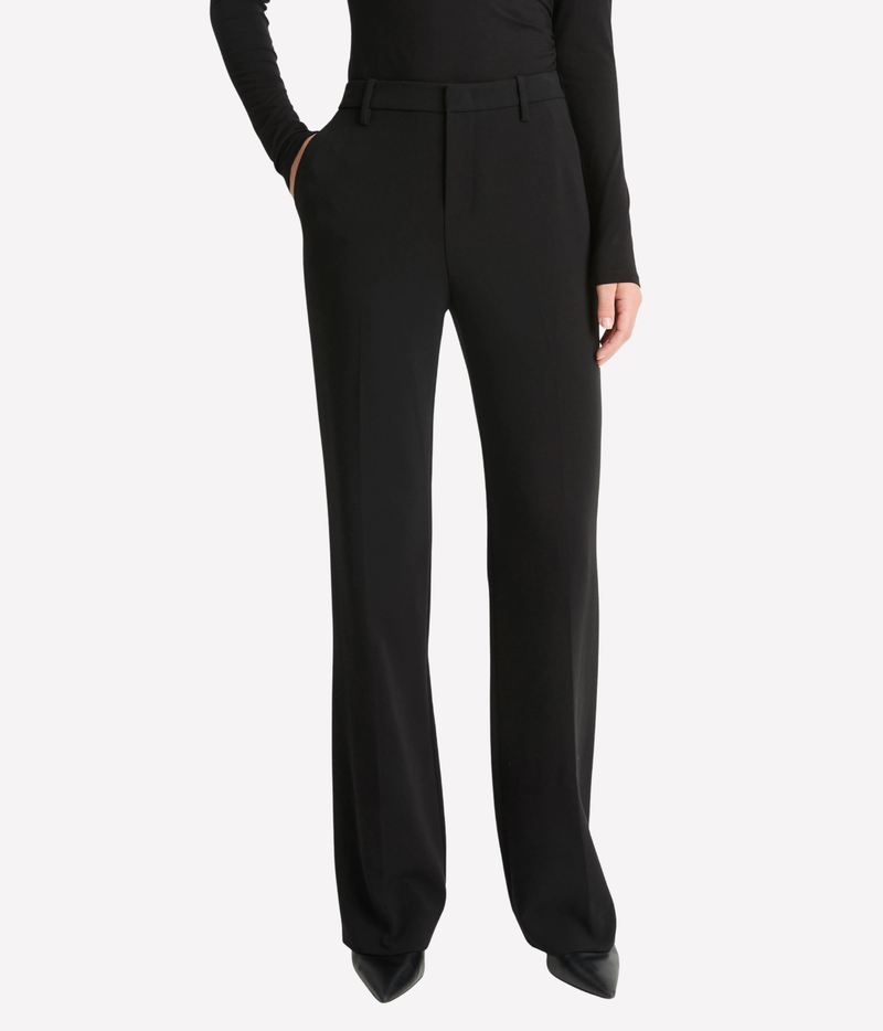 A model wearing black wide-leg trousers with a structured waistband, paired with a black long-sleeve top