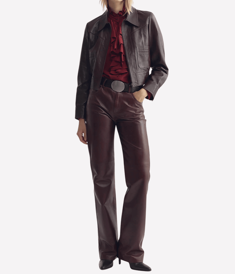 Full-length view of a model wearing the Nili Lotan Charly Leather Jacket in Bordeaux open over a red ruffled blouse with matching straight-leg leather trousers, a silver oval belt buckle and black pointed boots